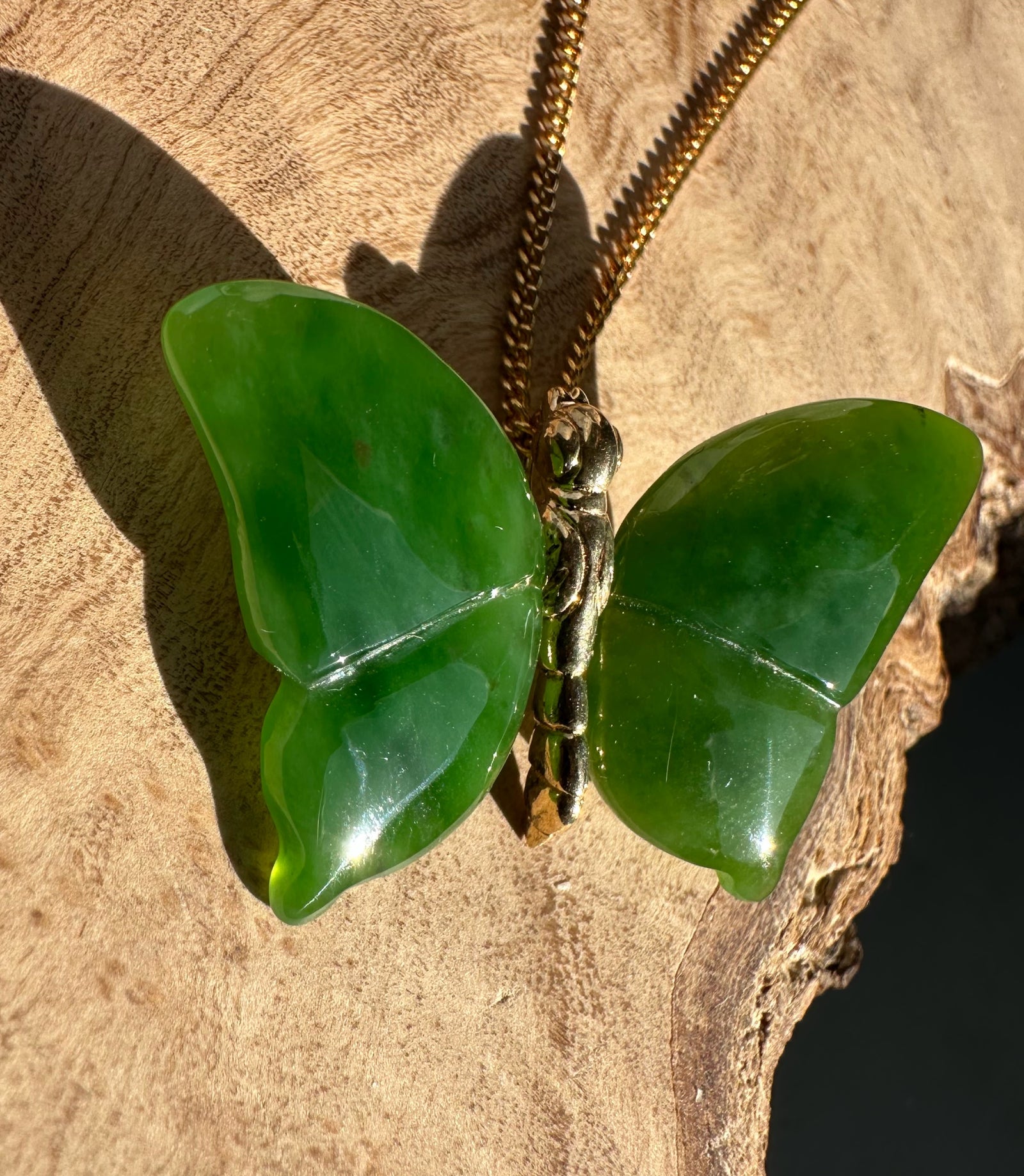 AA Grade Siberian Jade Butterfly Pendant on a gold chain resting on a natural rock surface