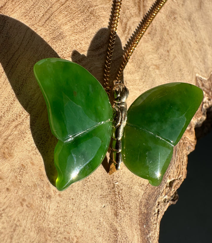 AA Grade Siberian Jade Butterfly Pendant on a gold chain resting on a natural rock surface