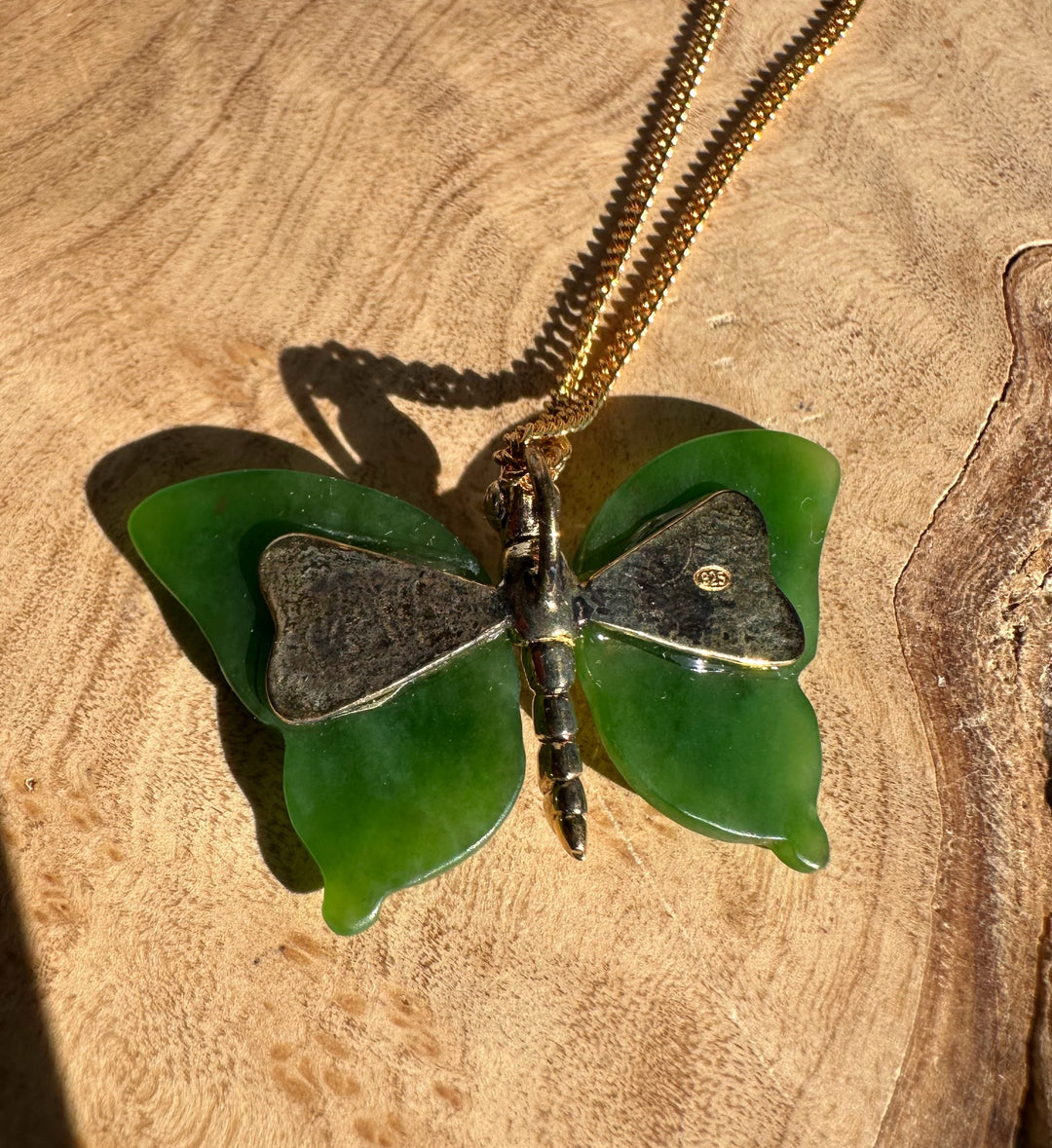 AA Grade Siberian Jade Butterfly Pendant on a gold chain resting on wood
