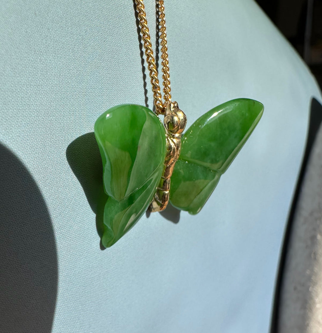 Green jade butterfly pendant with a gold chain against a light blue background