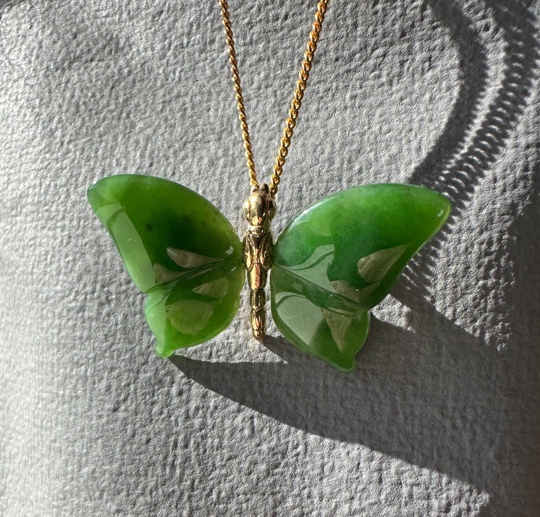 Green jade butterfly pendant with a gold chain viewed from above on a gray textured surface