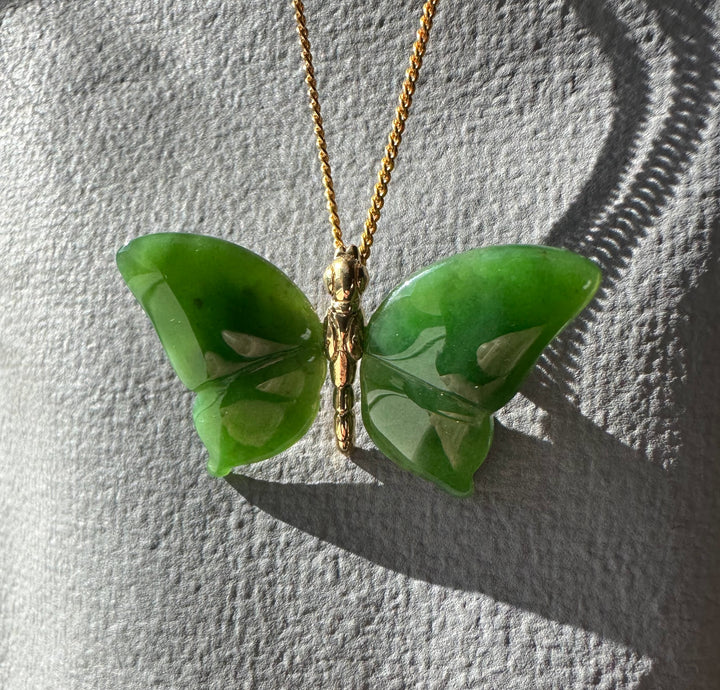 Green jade butterfly pendant with a gold chain viewed from above on a gray textured surface