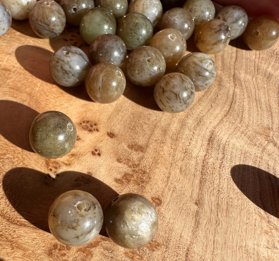 Loose round jade beads scattered on a wooden surface with natural veining