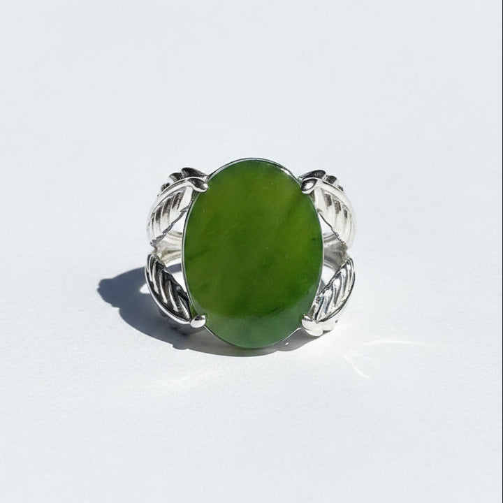 A silver ring with a large oval green jade, photographed on a white in natural sunlight.