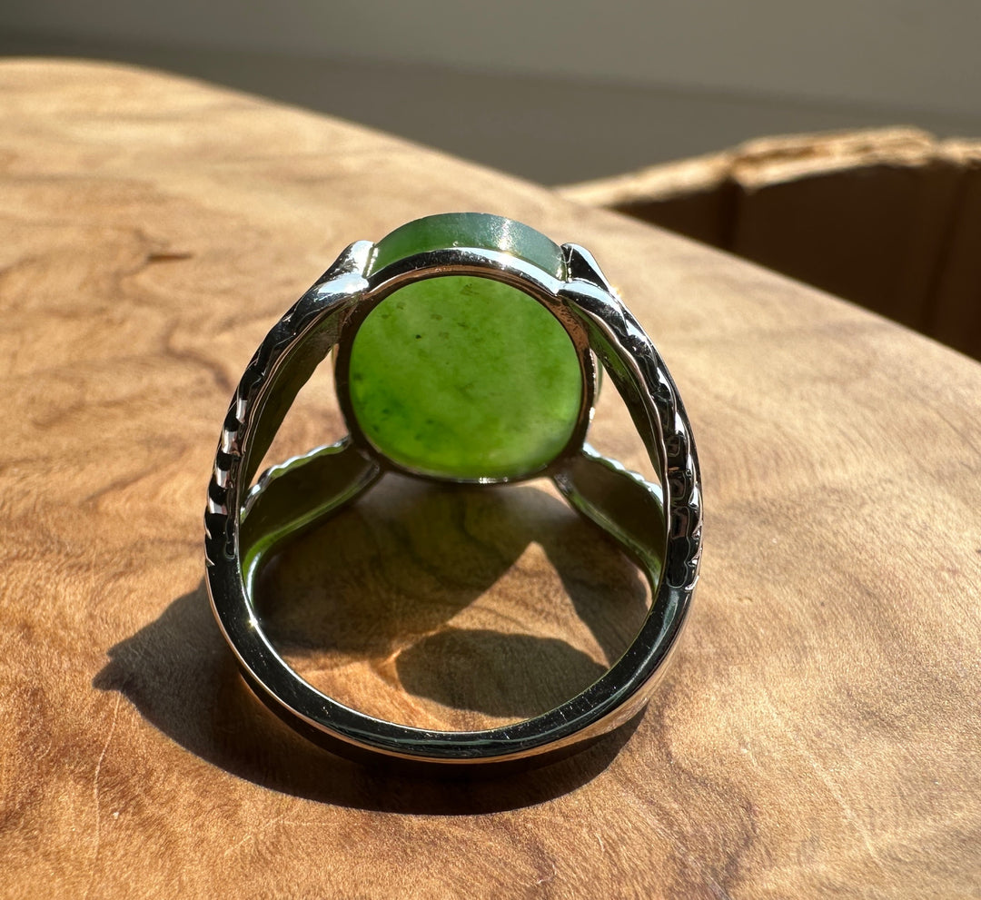 A sterling silver ring with a round green stone, resting on a textured wooden surface.