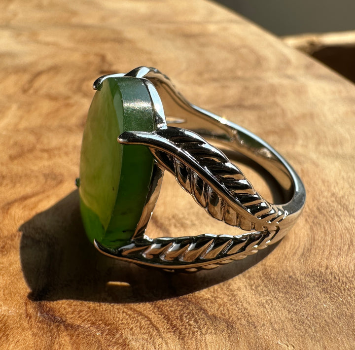 A sterling silver ring with a textured leaf-shaped band and a large green cabochon gemstone, resting on a rustic wooden surface.