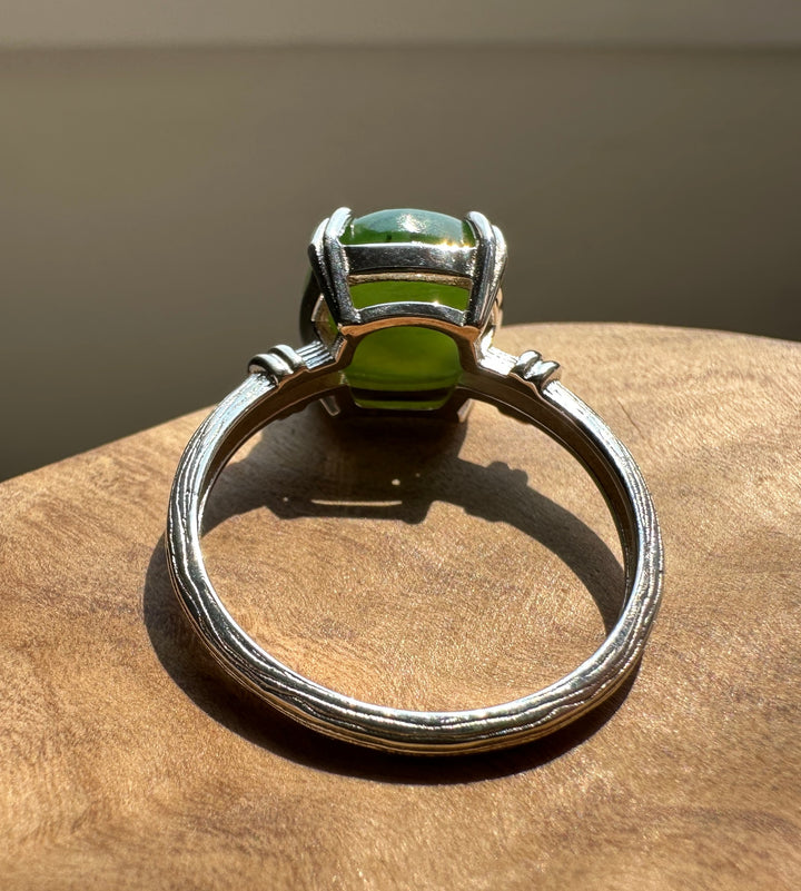 A silver ring with a green cabochon gemstone, resting on a textured wooden surface.