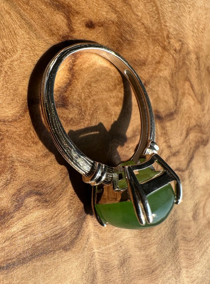 A sterling silver ring with a large, polished green gemstone in a prong setting, displayed on a textured brown wood background.