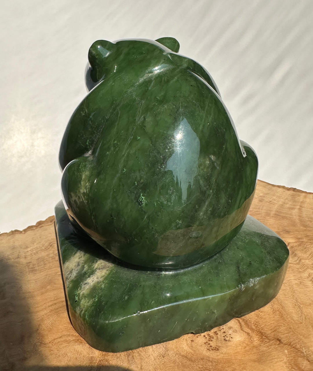 A polished green jade bear sculpture sitting on a wooden surface against a white background.