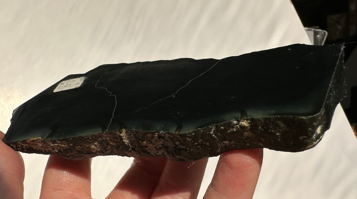 A raw, polished black jade stone slab held in a person&