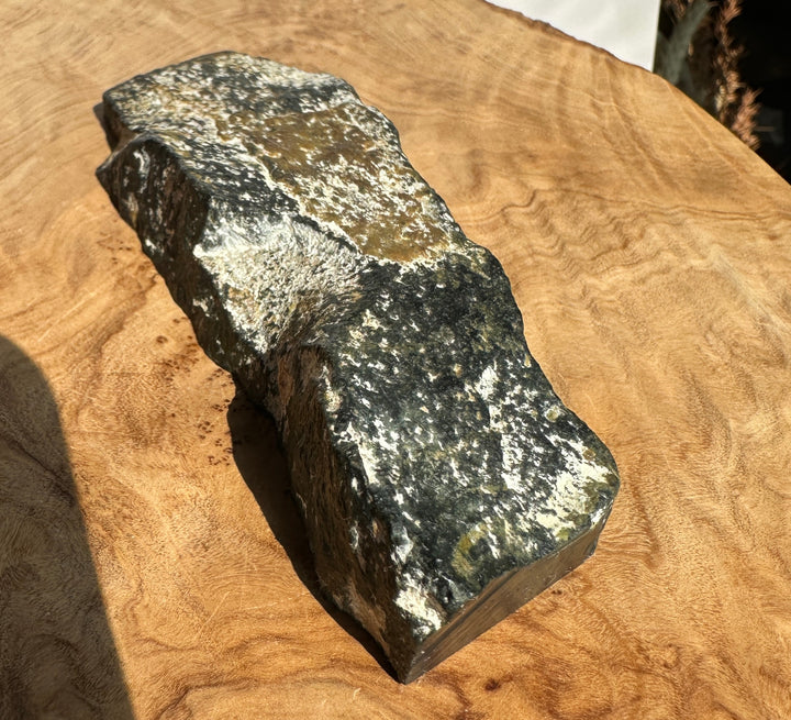 A rough, natural jade sample with a dark gray and black body and bright white crystalline patches, resting on a warm brown wood surface.