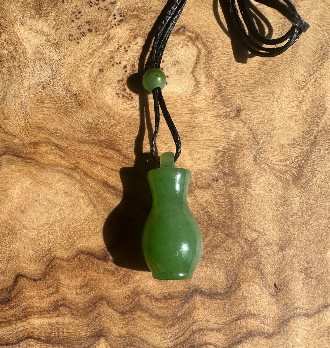 Green jade pendant with black cord on a wooden surface