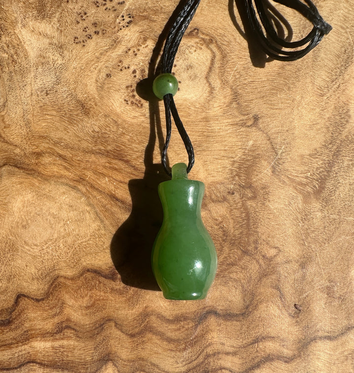 Green jade pendant with black cord on a wooden surface
