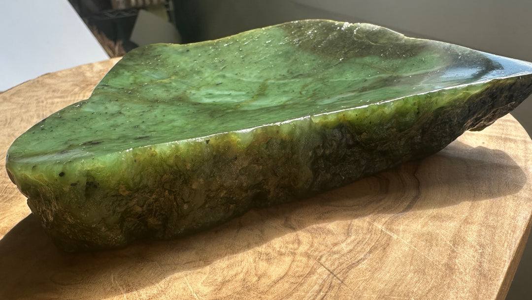 A polished green jade decorative slab with natural marbling, displayed on a round wooden cutting board.