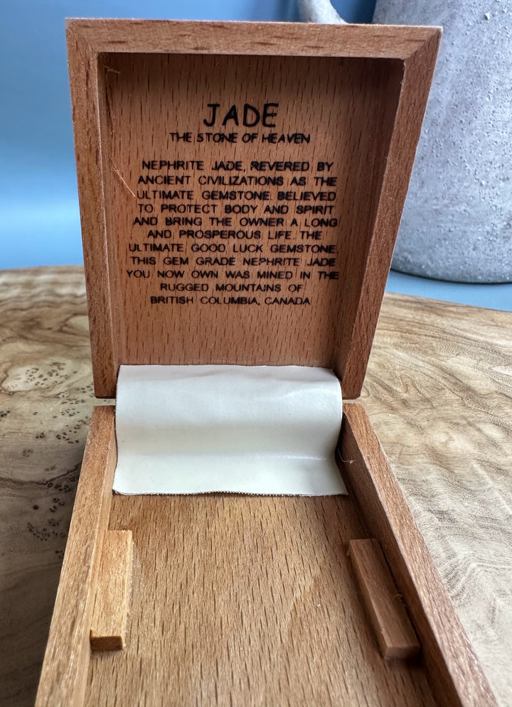 Open wooden box revealing Jade inscription on the lid and a white parchment inside.