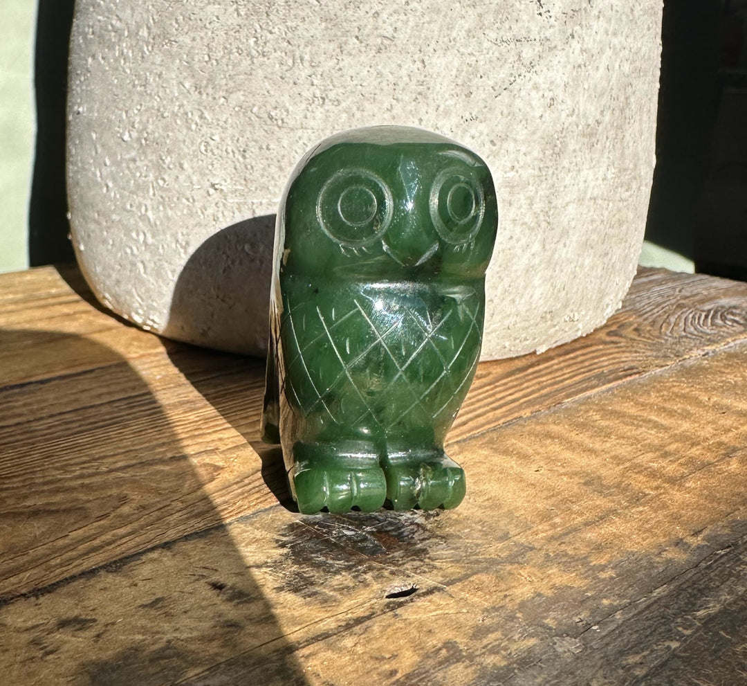 Front view of a 2-inch green Canadian jade owl with carved feather lines on a wooden surface