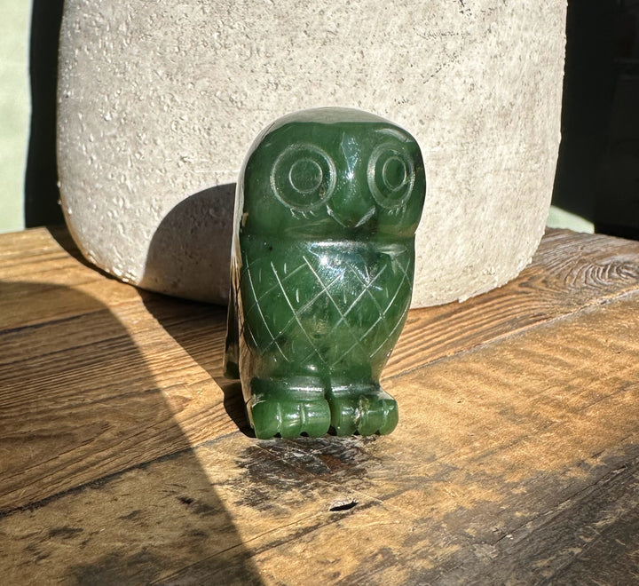 Front view of a 2-inch green Canadian jade owl with carved feather lines on a wooden surface