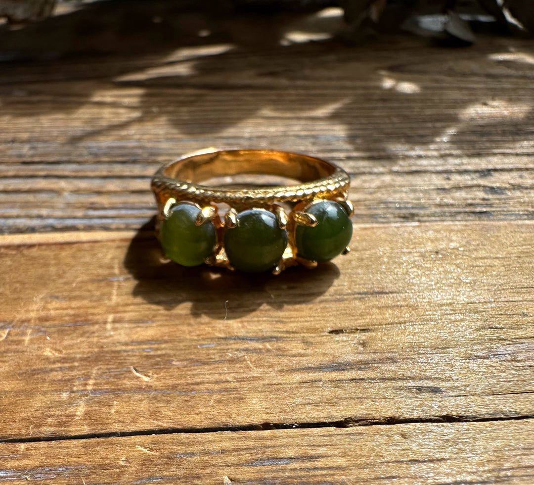 Gold ring with three round green jade beads along the band on a wooden surface