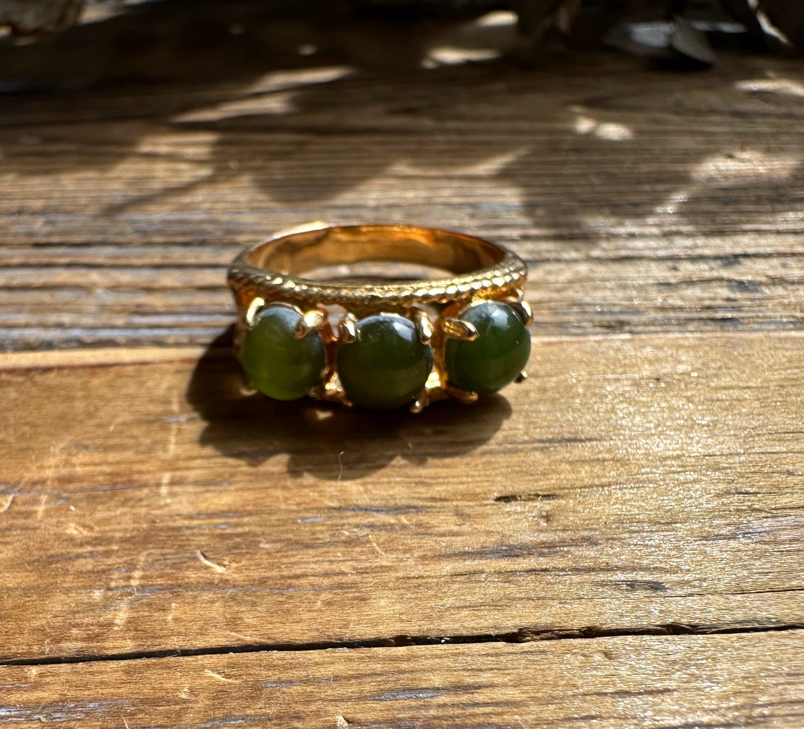 Gold ring with three round green jade beads along the band on a wooden surface