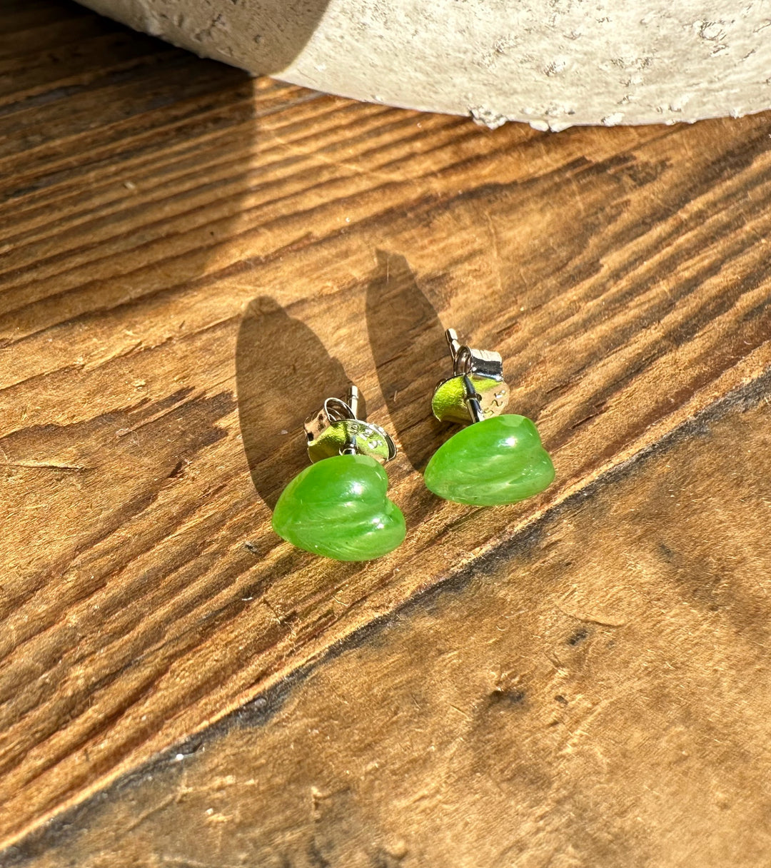 Pair of green heart shaped earrings with silver findings on rustic wood