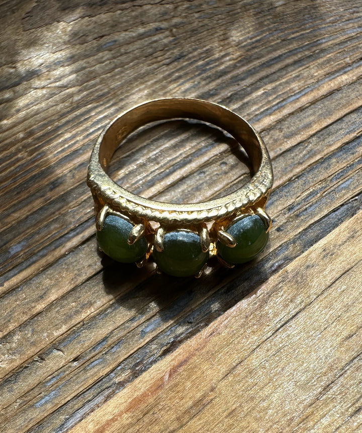 Gold ring featuring three green jade cabochons set in a row on a textured band on a wooden surface