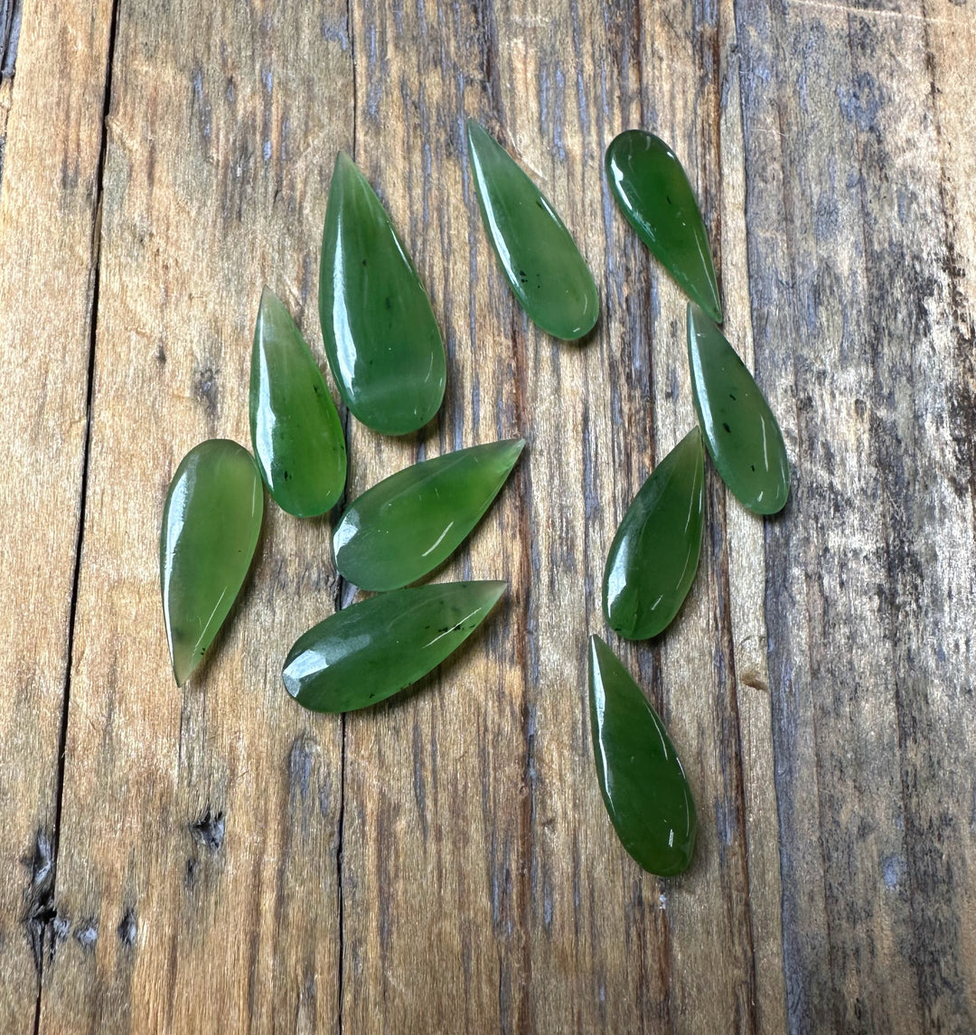 Several green teardrop cabochons scattered on a rustic wooden board