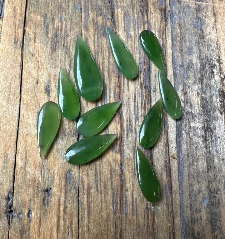 Several green teardrop cabochons scattered on a rustic wooden board