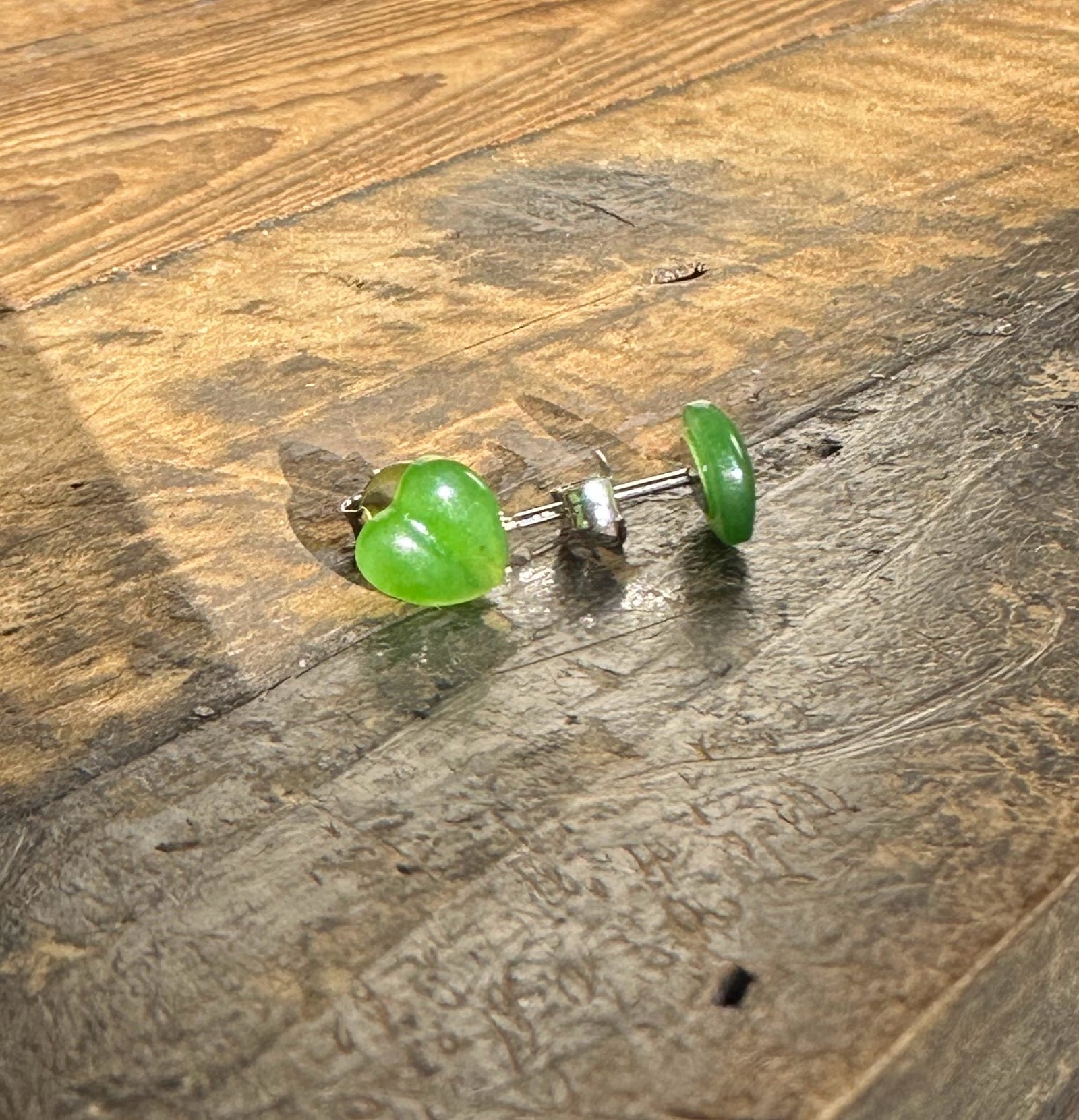 Heart shaped green jade earrings with silver posts 7x8 mm on a wood surface