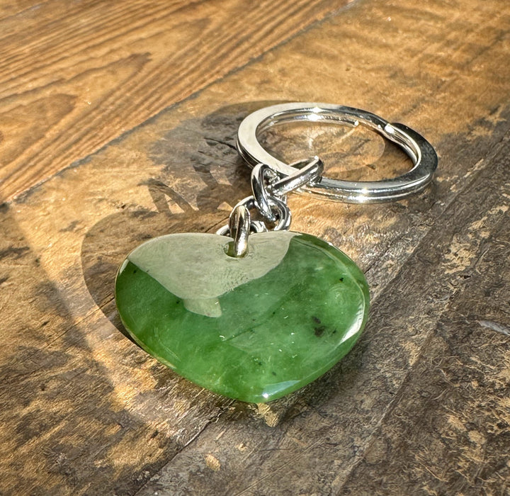 Green heart shaped stone keychain with a metal ring resting on a wooden surface