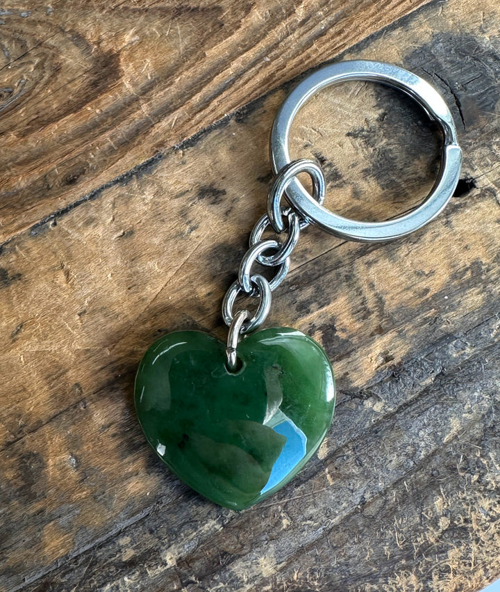 Green polished heart shaped keychain pendant attached to a silver chain and ring on a rustic wood surface.