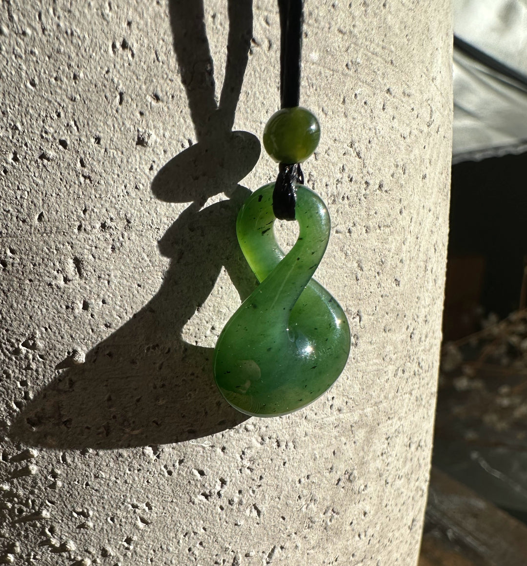 Jade infinity twist pendant hung on cord against a textured concrete surface in sunlight