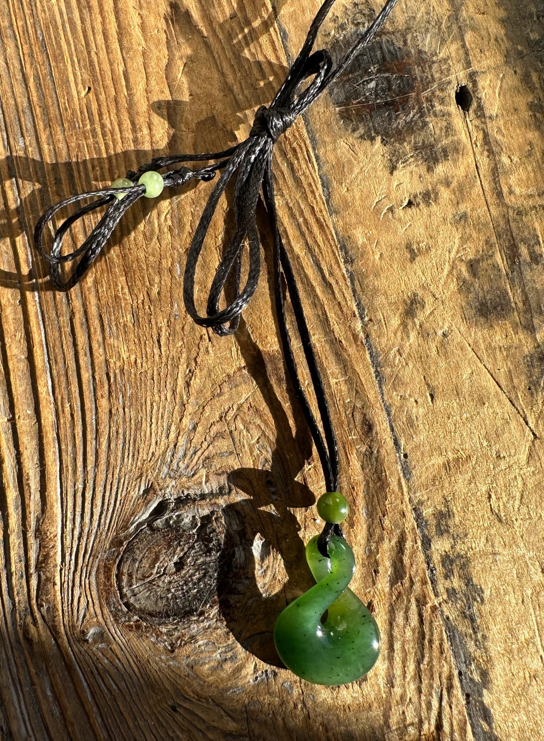 Close-up of jade infinity twist pendant on black cord resting on a wooden surface.