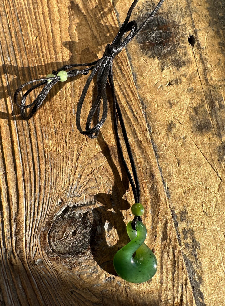 Close-up of jade infinity twist pendant on black cord resting on a wooden surface.