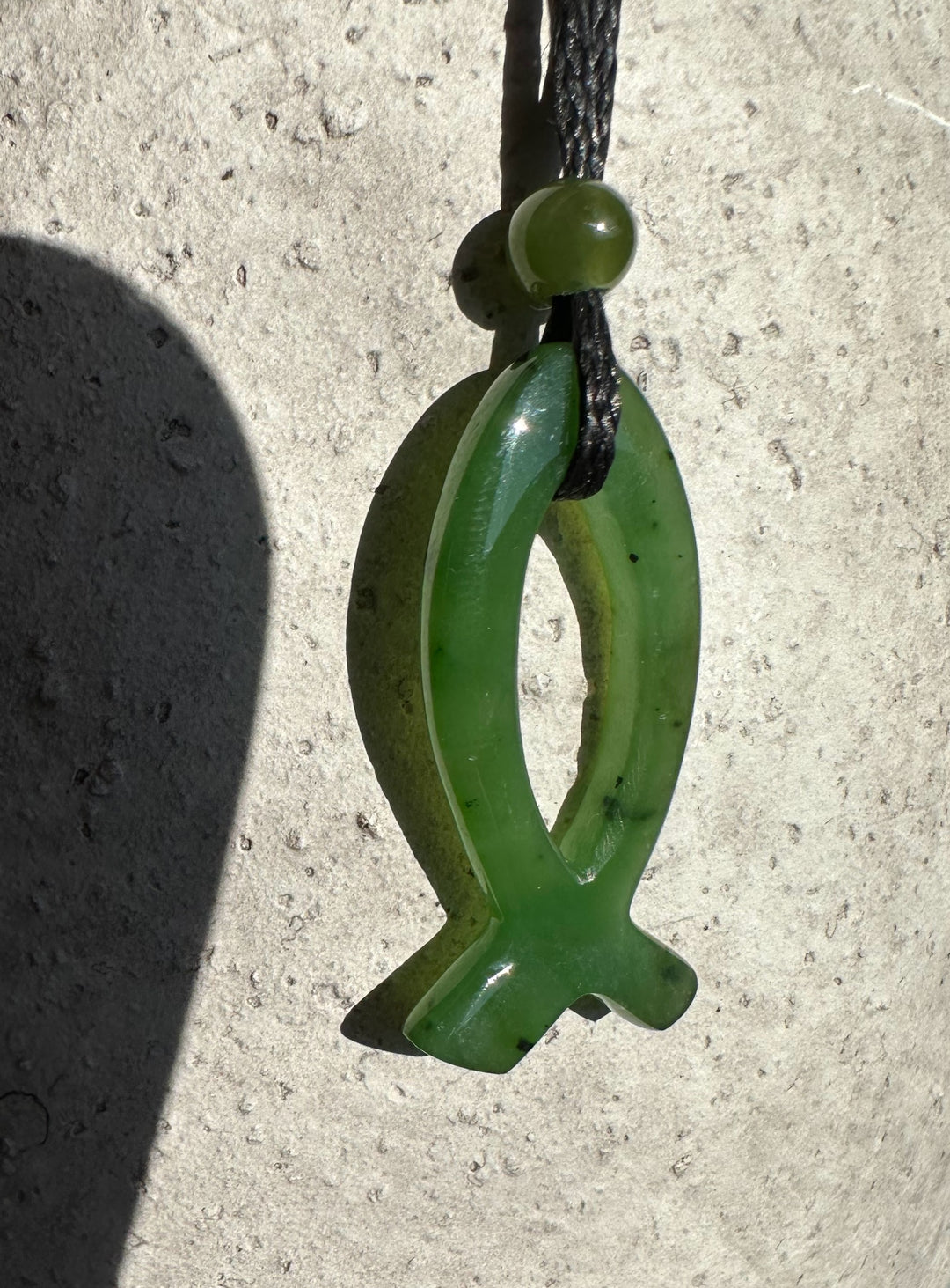 Close up of 30mm green jade Ichthys pendant with oval loop and cross tail on a black cord.