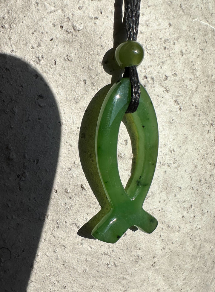 Close up of 30mm green jade Ichthys pendant with oval loop and cross tail on a black cord.
