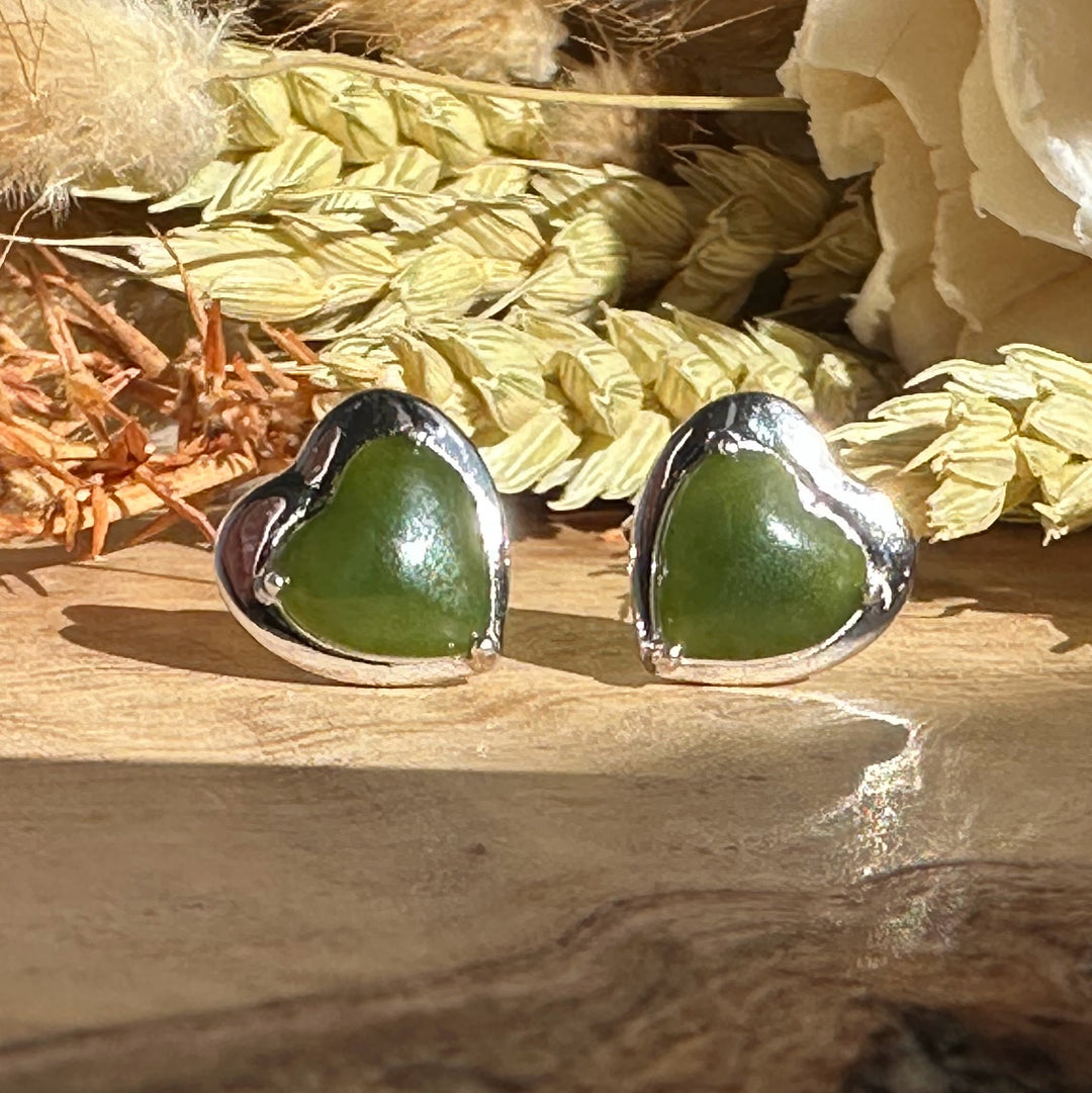 Pair of silver heart earrings with green heart shaped stones on a wooden surface.