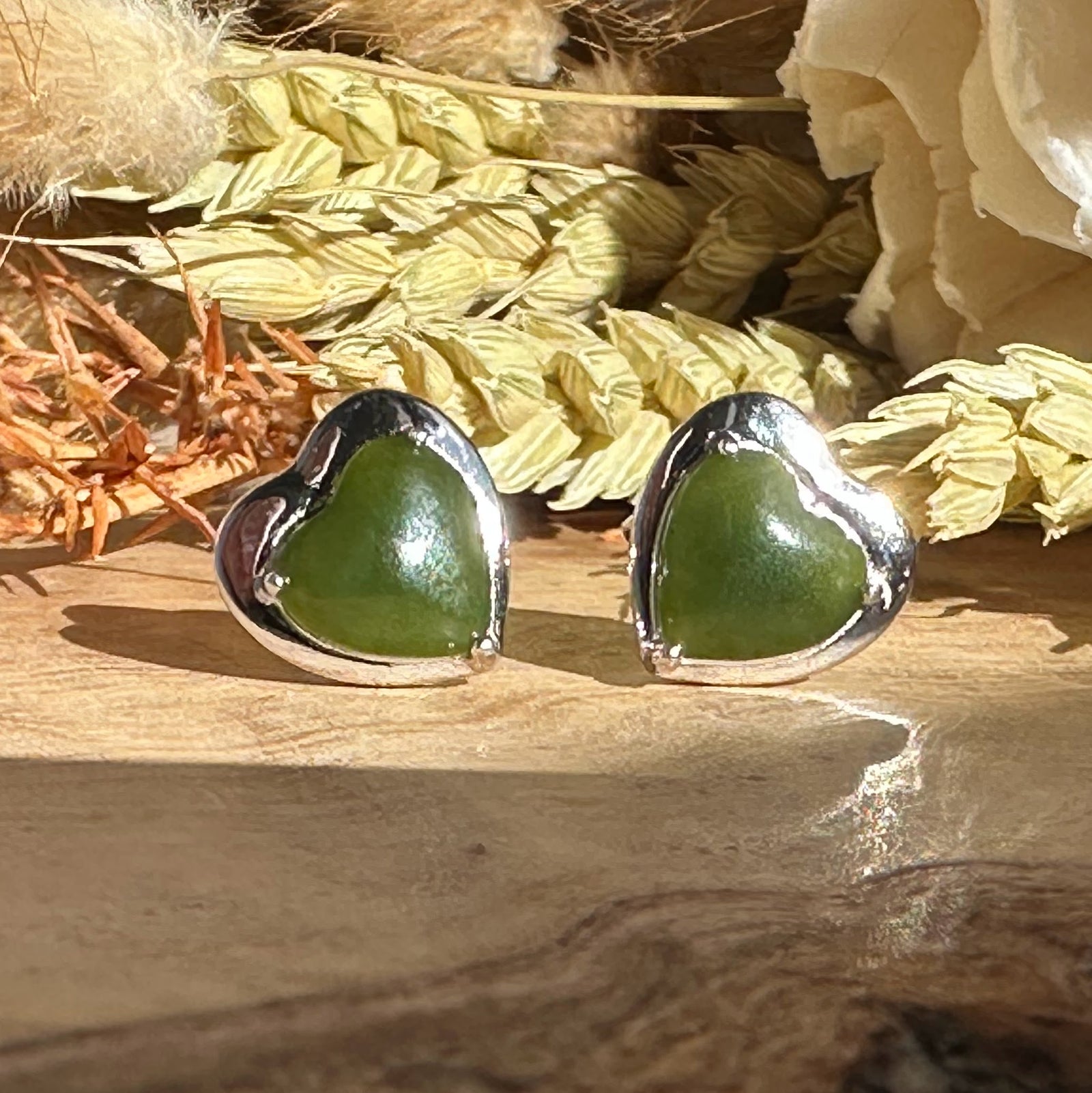 Pair of silver heart earrings with green heart shaped stones on a wooden surface.