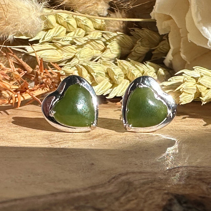 Pair of silver heart earrings with green heart shaped stones on a wooden surface.