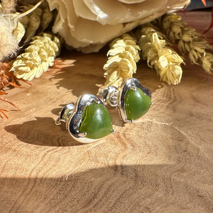 Close-up of silver heart stud earrings with green stones on a wooden surface.