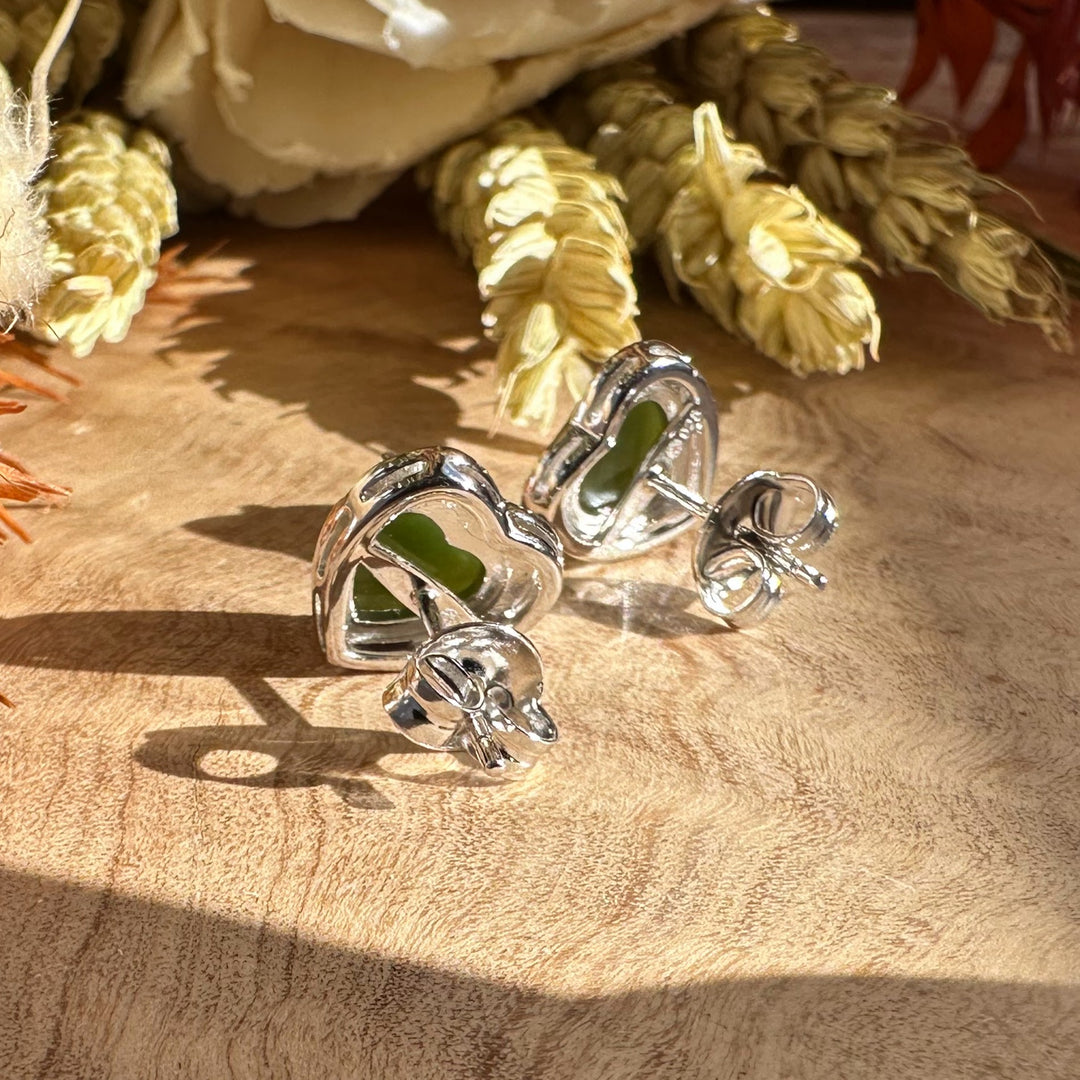 Silver heart earrings with green stones resting on a wooden surface