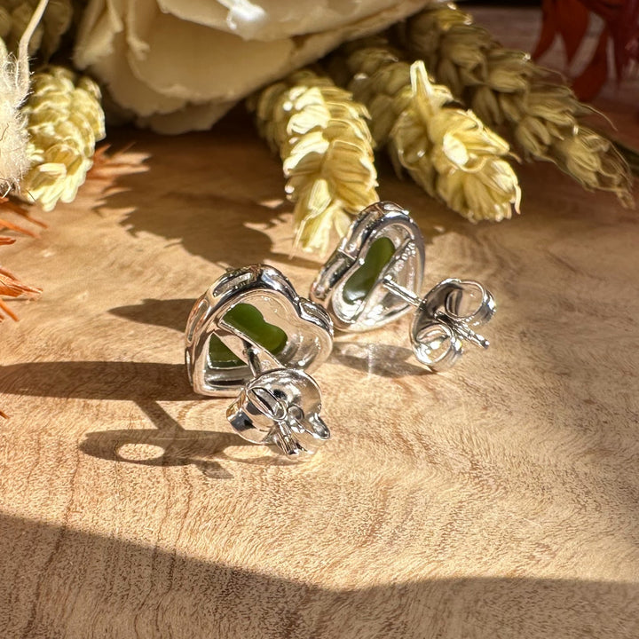 Silver heart earrings with green stones resting on a wooden surface