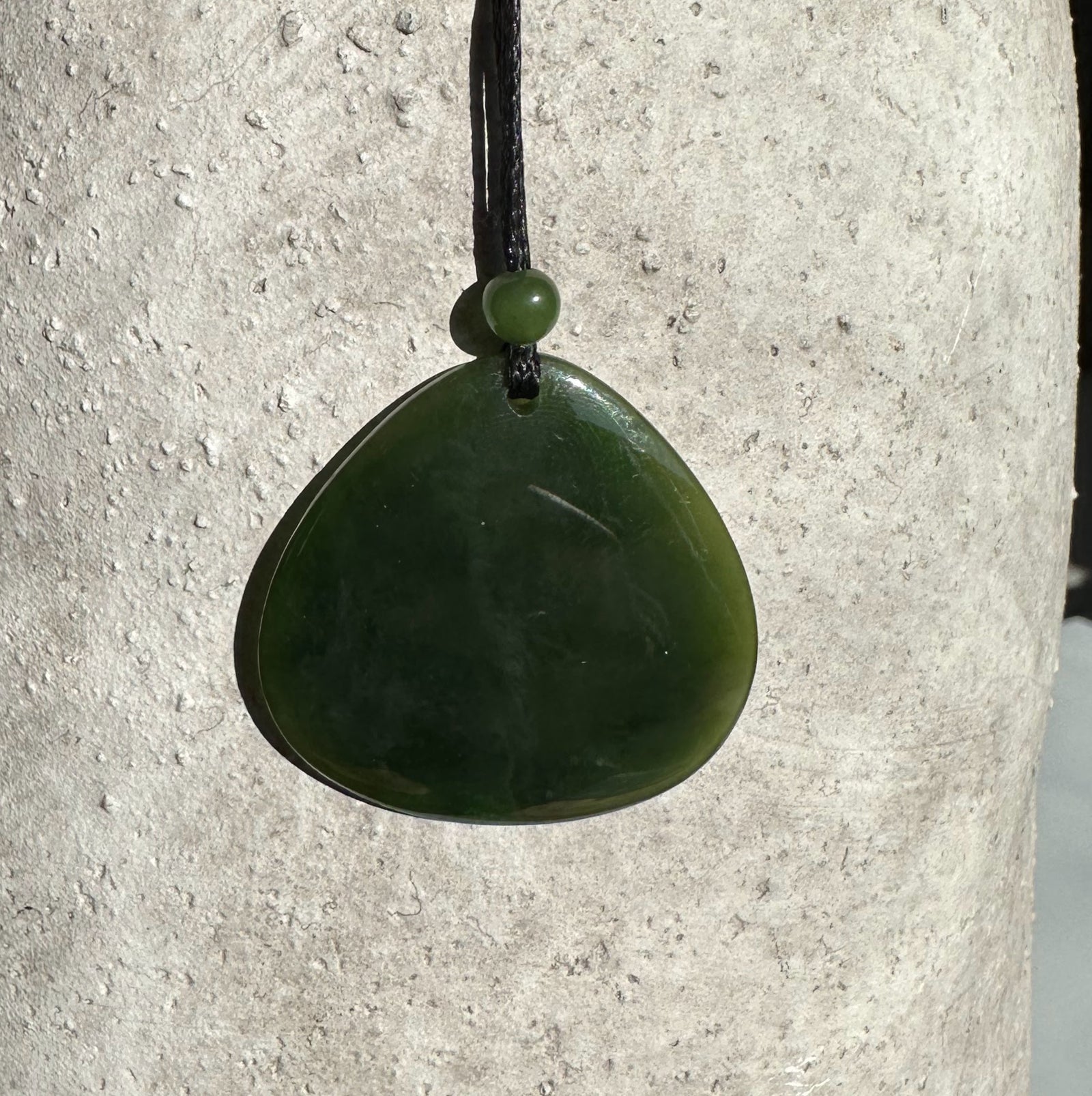 Dark green jade teardrop pendant suspended from a black cord with a small bead above it
