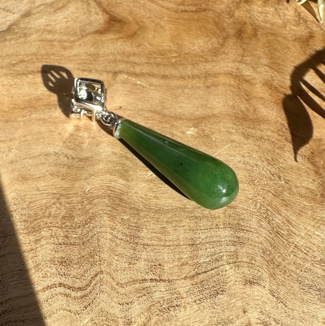 Canadian nephrite green jade teardrop pendant with silver cap on wood background