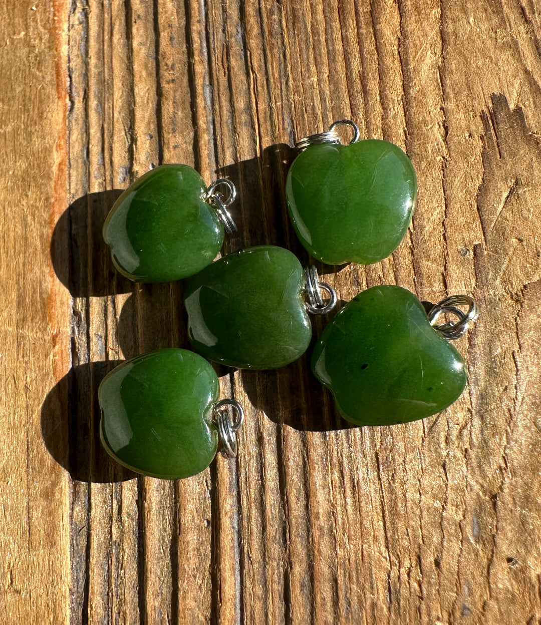 Green jade Apple Charm pendant with silver bail on a wooden background