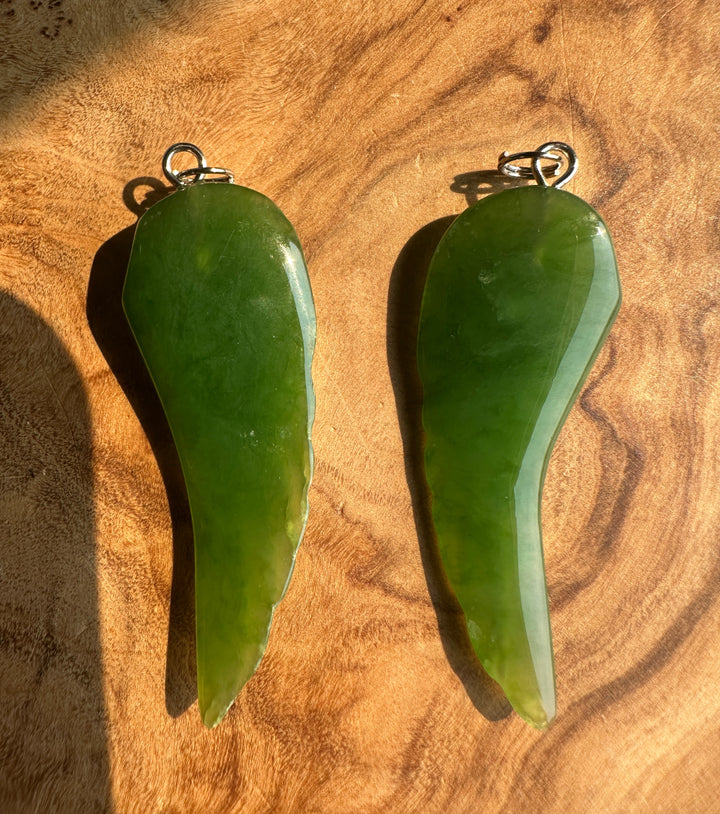 Two green jade pendants with silver jump rings, displayed on a textured wooden surface.