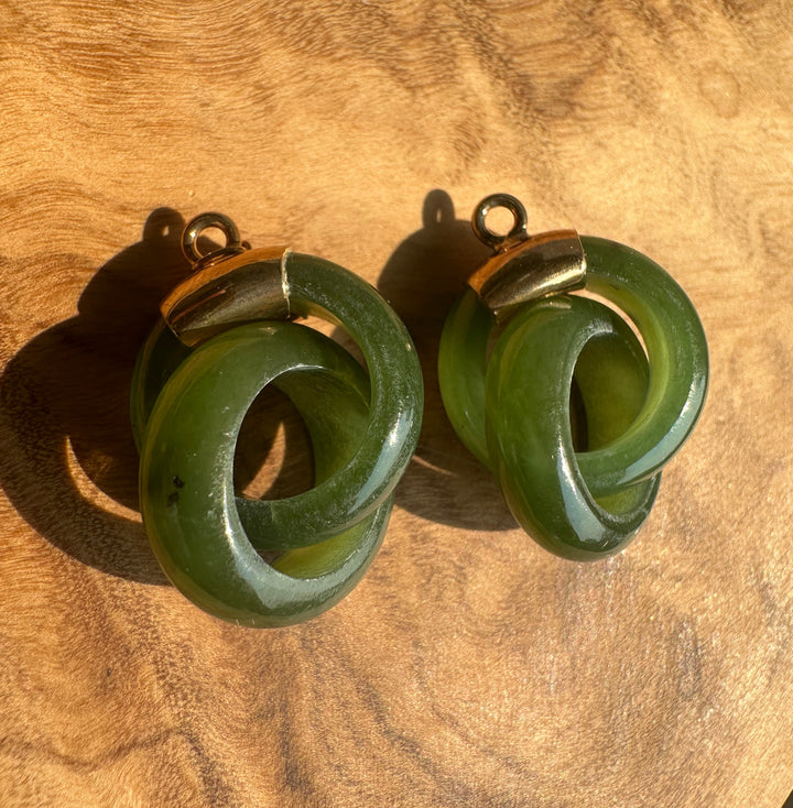 A pair of green interlocking ring earrings with gold-toned metal caps and loops, displayed on a textured wooden surface.