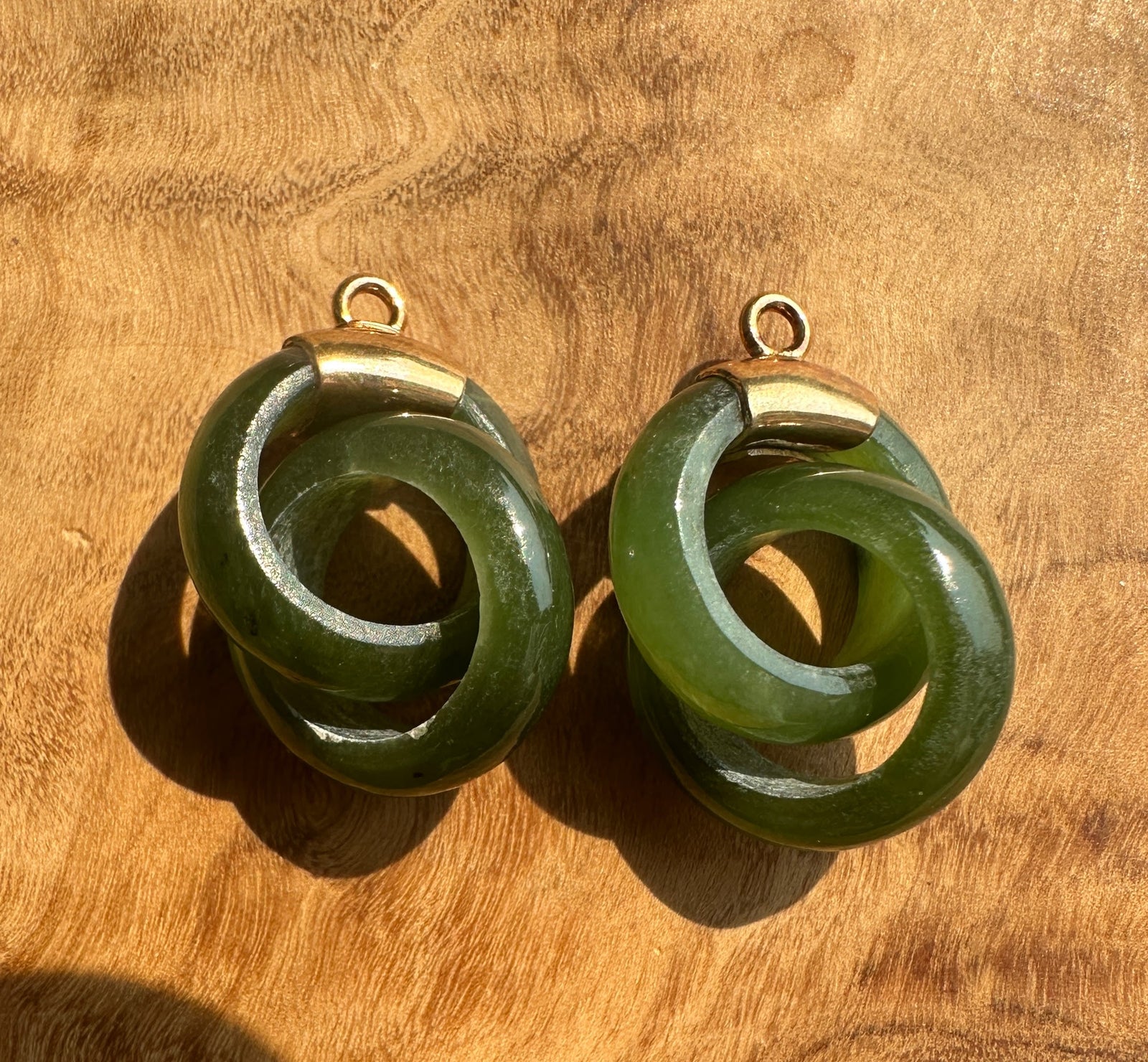 A pair of green interlocking rings with gold-tone metal caps and loops, displayed on a warm wooden surface.