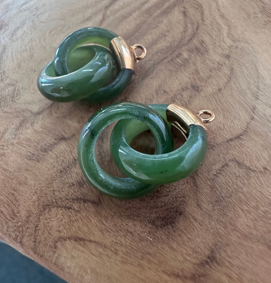 A pair of green interlocking ring with gold-tone metal caps and loops, displayed on a wooden surface.