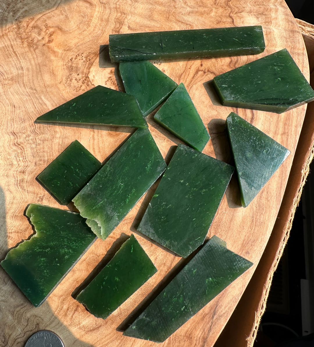 Several dark green rectangular and triangular blocks of solid material, jade, scattered on a light brown wood slice background.