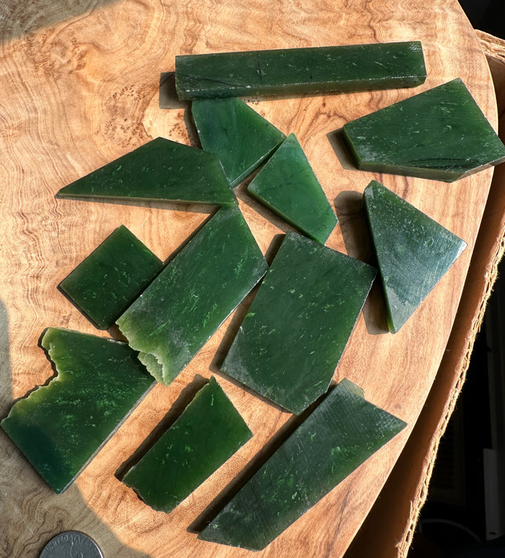Several dark green rectangular and triangular blocks of solid material, jade, scattered on a light brown wood slice background.